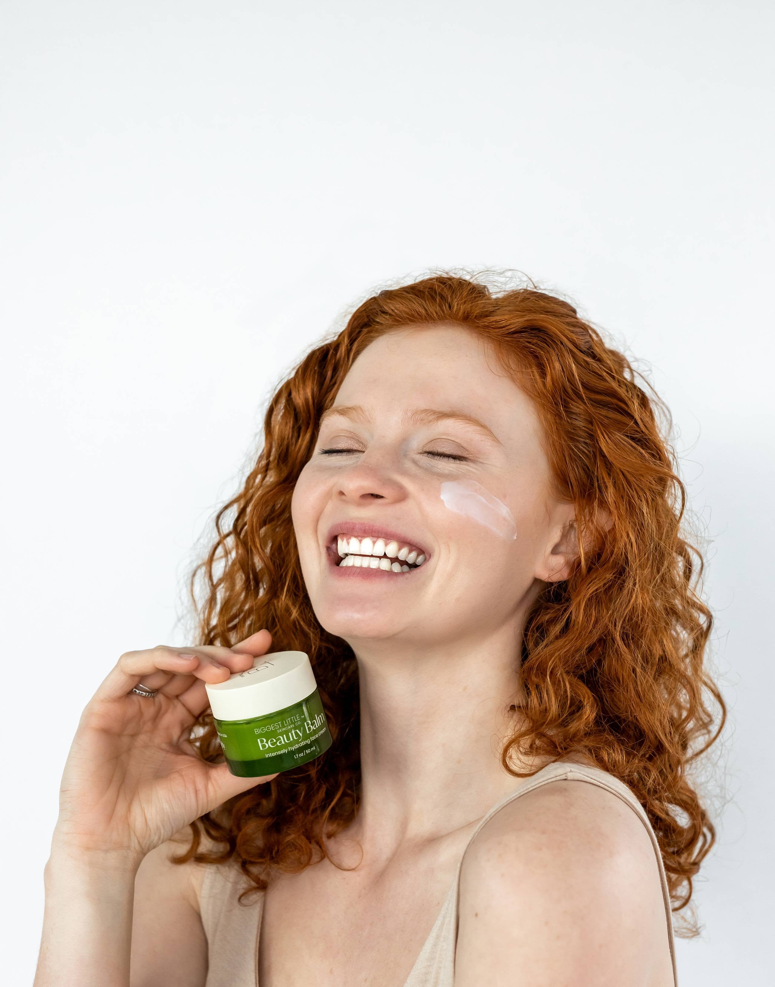 red head young woman smiling while holding the Beauty Balm on her hand